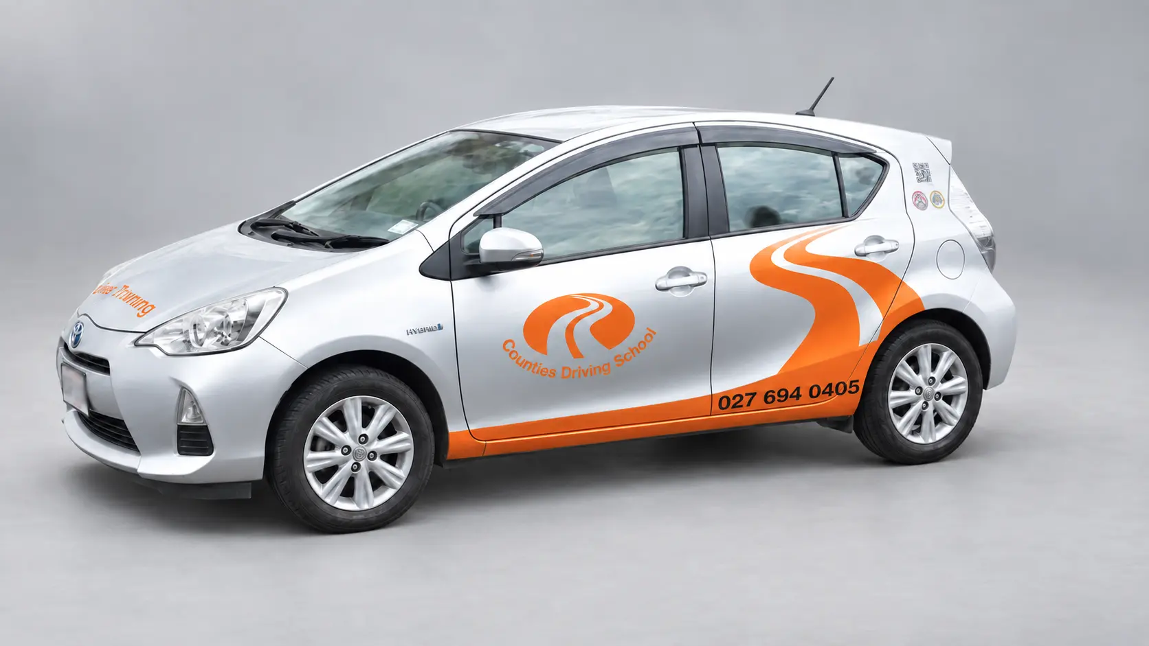 Silver Counties Driving School Toyota Aqua with orange branding, viewed from the front and side.